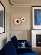 A dusky pink Clérachic wall light paired with a smaller white one on a panelled wall, near a blue armchair.