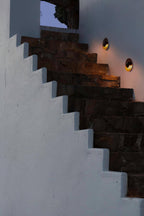 A single Clérachic wall light glows warm on a stone stairwell wall, set against a night sky.