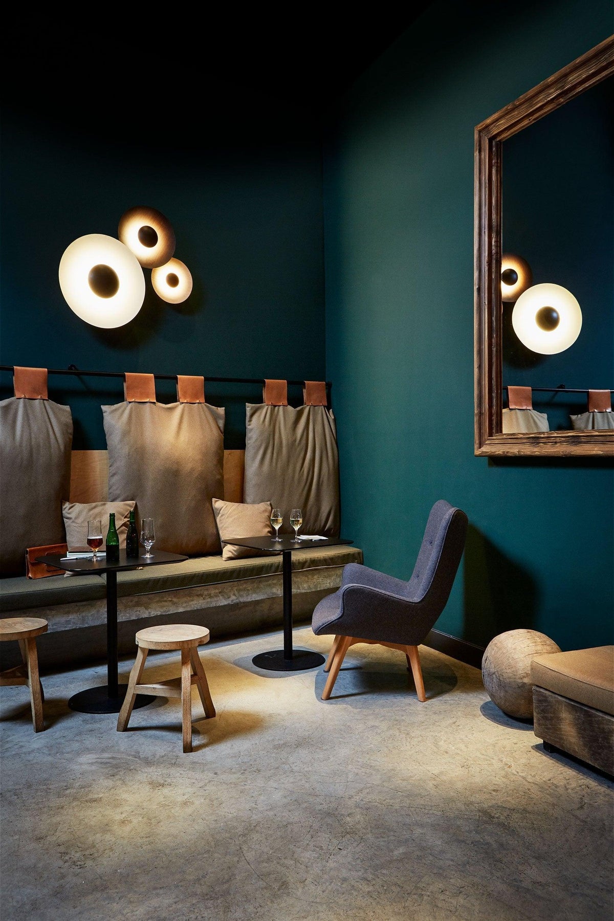Two Clérachic wall lights glow warm on a dark teal wall, reflected in an arched mirror beside a lounge seating area.