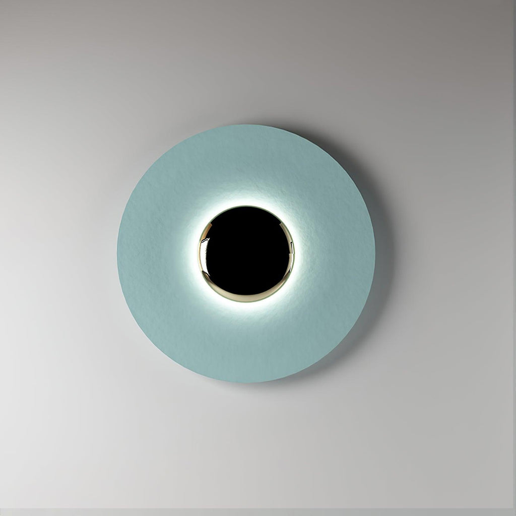 A pale blue Clérachic wall light on a plain grey backdrop, its black centre ringed by a soft glow.