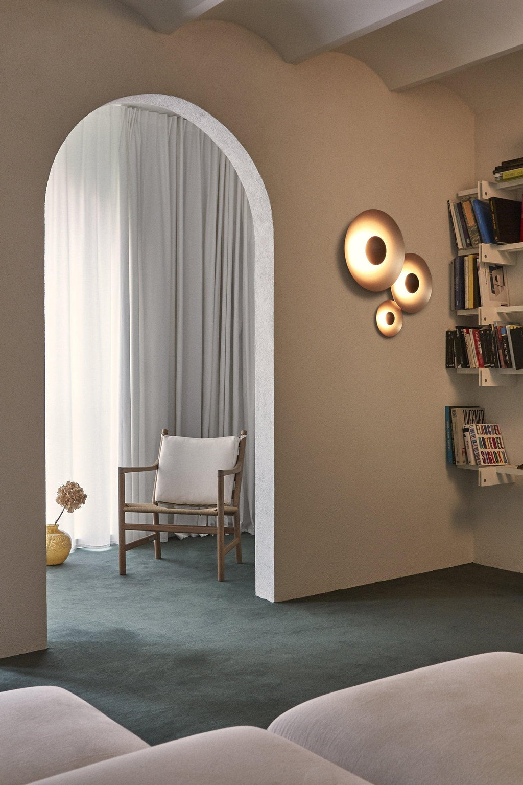 Grouped Clérachic wall lights glow warm beside an archway leading to a room with bookshelves and a wooden chair.