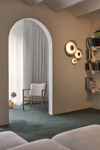 Grouped Clérachic wall lights glow warm beside an archway leading to a room with bookshelves and a wooden chair.