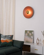 This orange Clérachic wall light glows above a console table, its antique copper centre bright, beside a framed print.