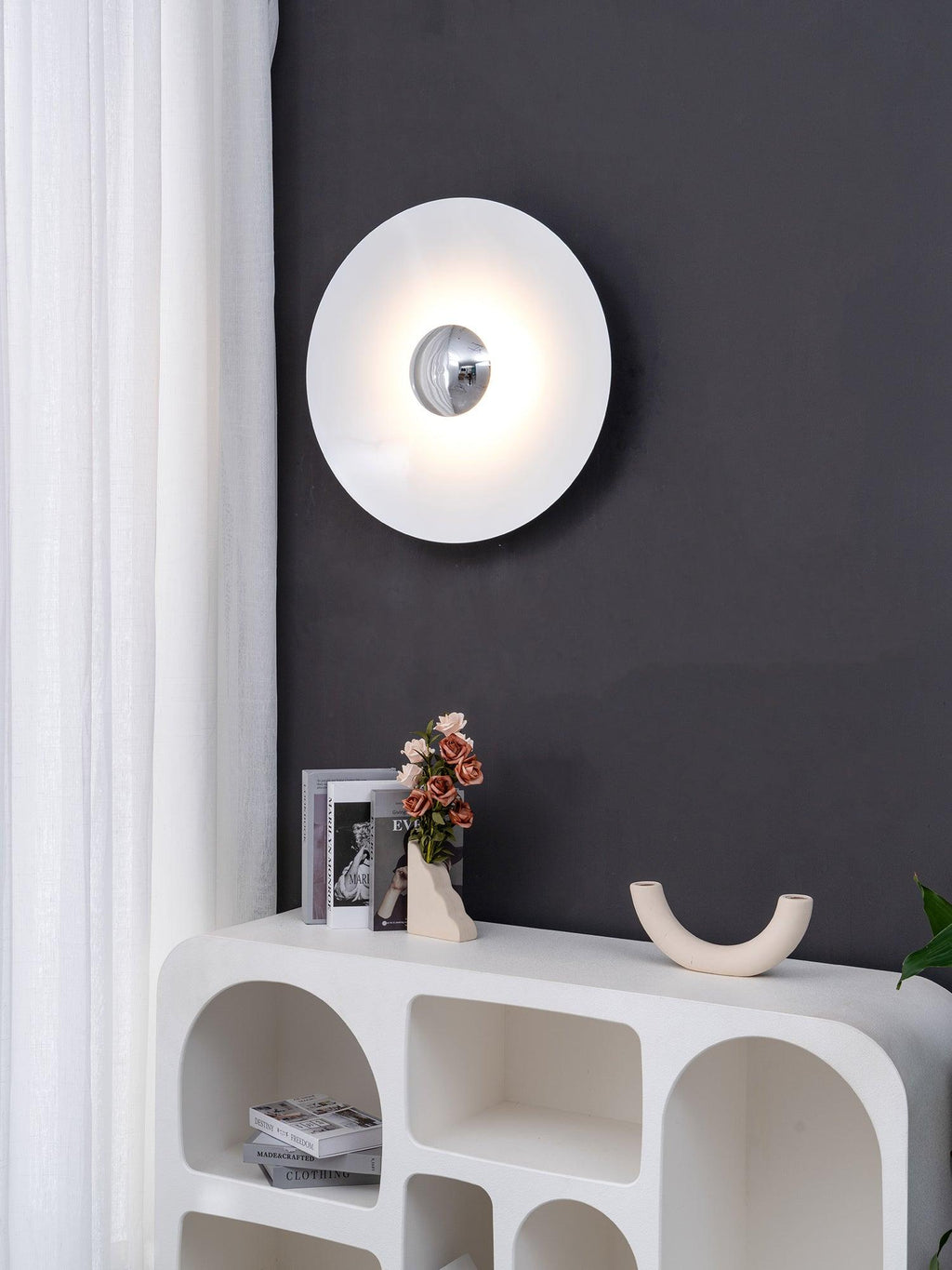 Closer view of the white Clérachic wall light glowing above a console table with books, on a charcoal wall.
