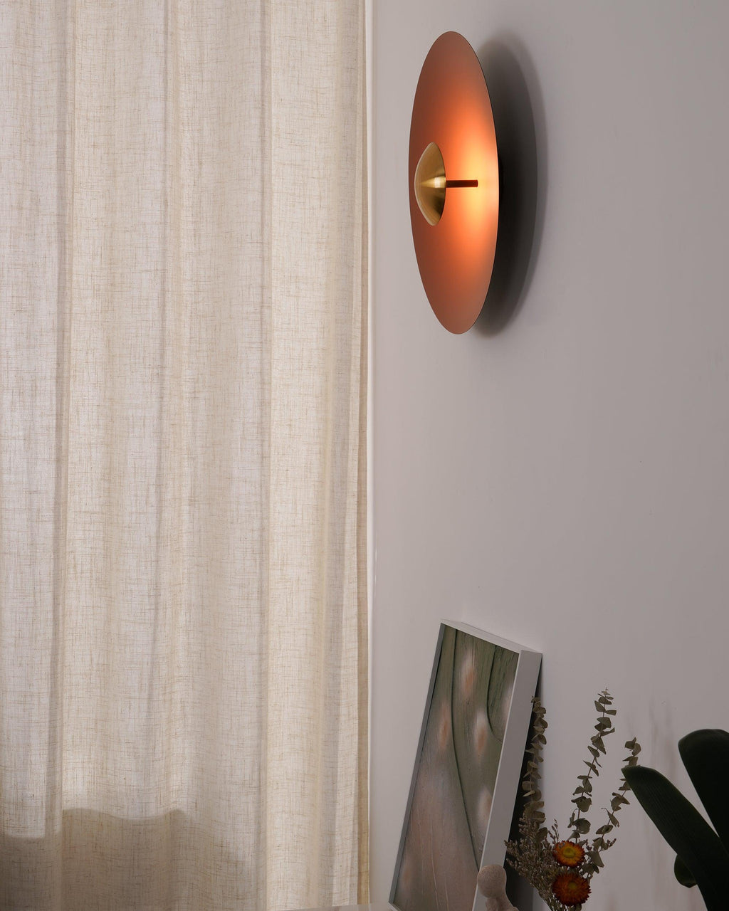 Side view of this orange Clérachic wall light showing its slim profile, mounted near a sheer curtain.