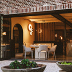 Two of this Clérachic wall light glow warm near a brick archway leading into a restaurant with a round table.