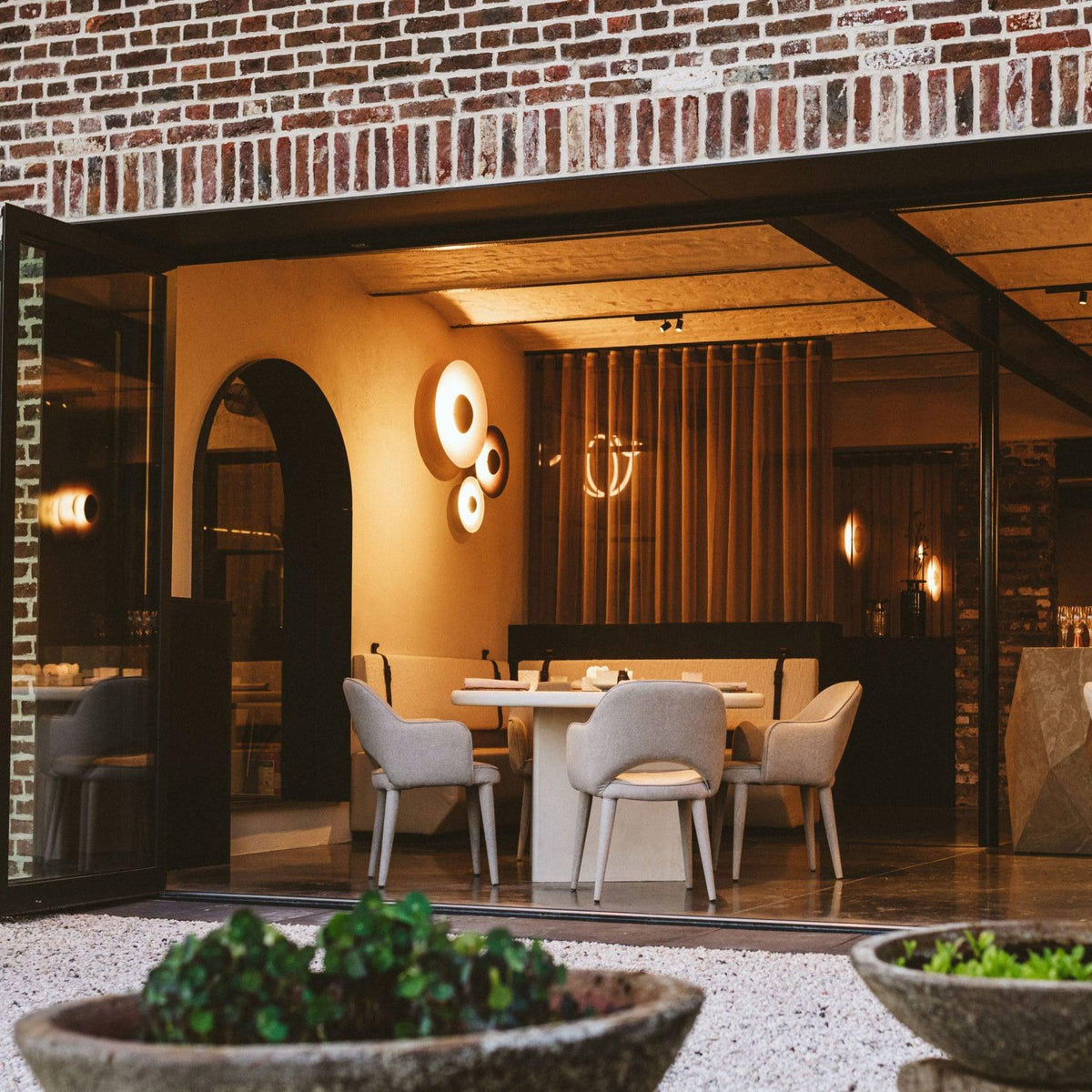Two of this Clérachic wall light glow warm near a brick archway leading into a restaurant with a round table.
