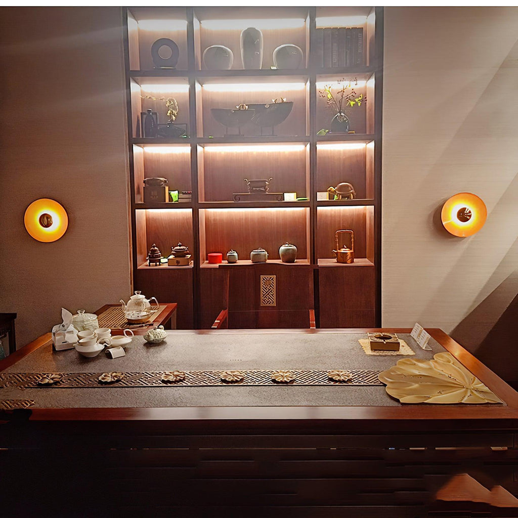 Two small Clérachic wall lights glow amber beside a lit shelving unit filled with teapots in a tea room.