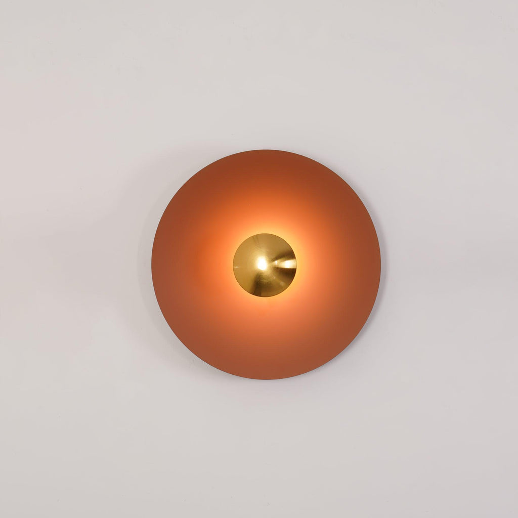 An unlit terracotta Clérachic wall light on a plain beige backdrop, its brass centre catching the light.