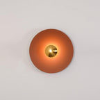 An unlit terracotta Clérachic wall light on a plain beige backdrop, its brass centre catching the light.