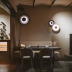 Three of this Clérachic wall light on a beige wall, two glowing pale and one dark, above restaurant booth seating.
