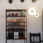 Two white Clérachic wall lights glow beside a rustic shelf holding copper pots and wine bottles.