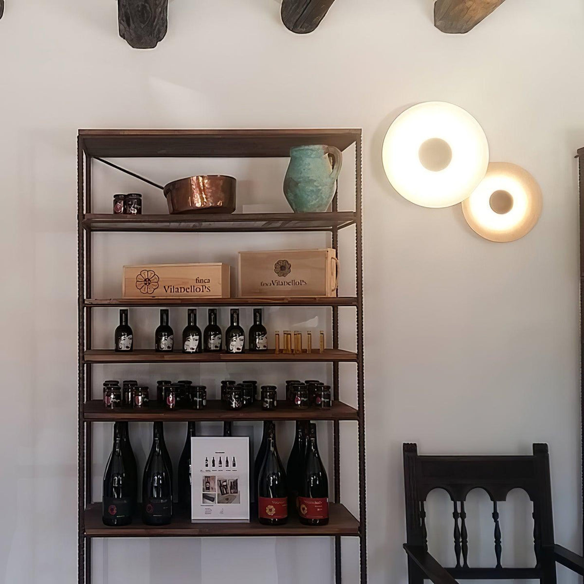 Two white Clérachic wall lights glow beside a rustic shelf holding copper pots and wine bottles.