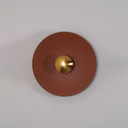 Closer angled view of the unlit terracotta Clérachic wall light on a grey wall, its brass centre in shadow.