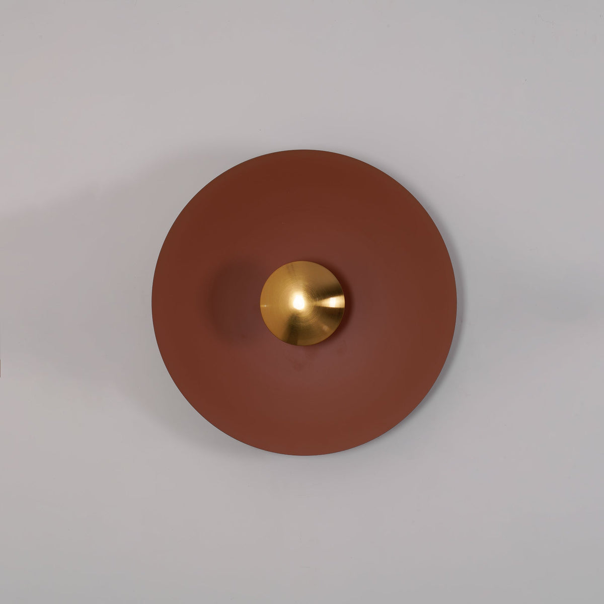 Closer angled view of the unlit terracotta Clérachic wall light on a grey wall, its brass centre in shadow.