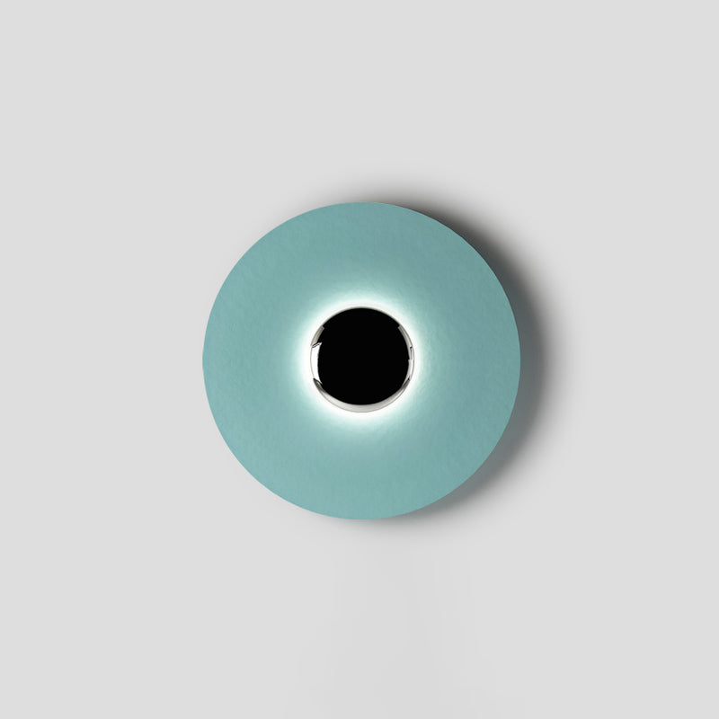 Slightly off-centre in the frame, this pale aqua Clérachic wall light glows softly around a black circular core.