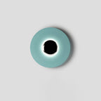 Centred on a plain grey backdrop, this pale aqua Clérachic wall light shows a soft ring of light around its black core.