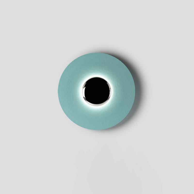 Centred on a plain grey backdrop, this pale aqua Clérachic wall light shows a soft ring of light around its black core.