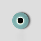 A tighter crop shows the pale aqua Clérachic wall light on grey, light glowing evenly around its black centre.