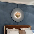 A pale grey Clérachic wall light glows above a bed with a leather headboard, on a slate-blue panelled wall.