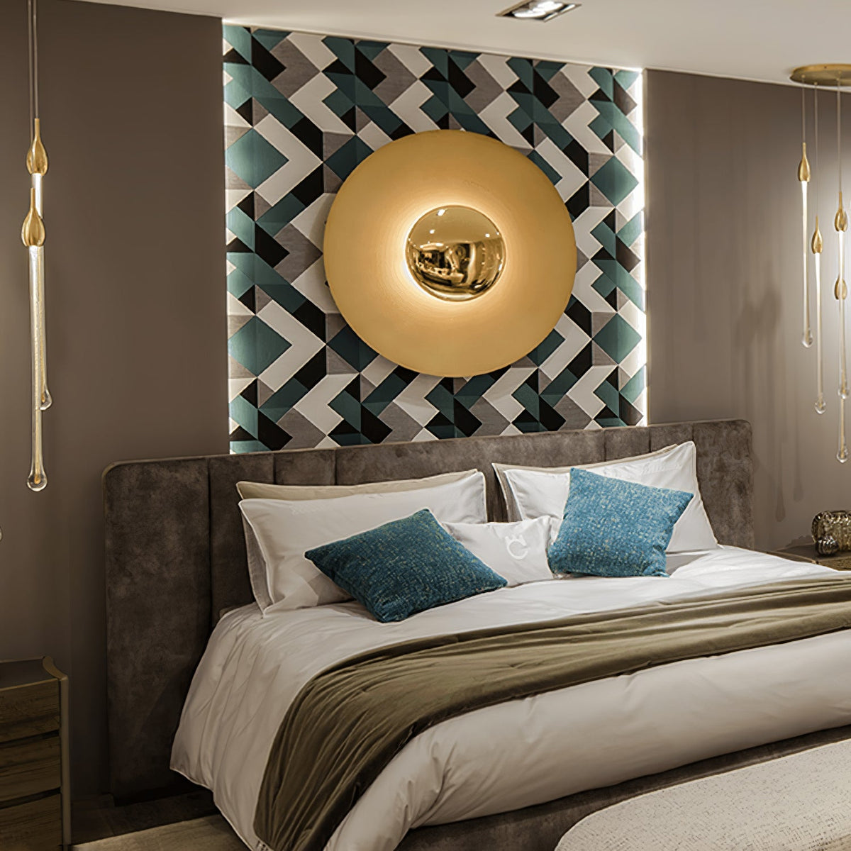 A brass-toned Clérachic wall light glows above a bed with teal cushions, set against a geometric patterned wall panel.