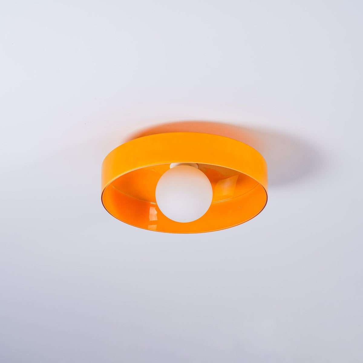 This Clérachic orange ceiling light at an angle, its shade casting a soft shadow on the backdrop behind.