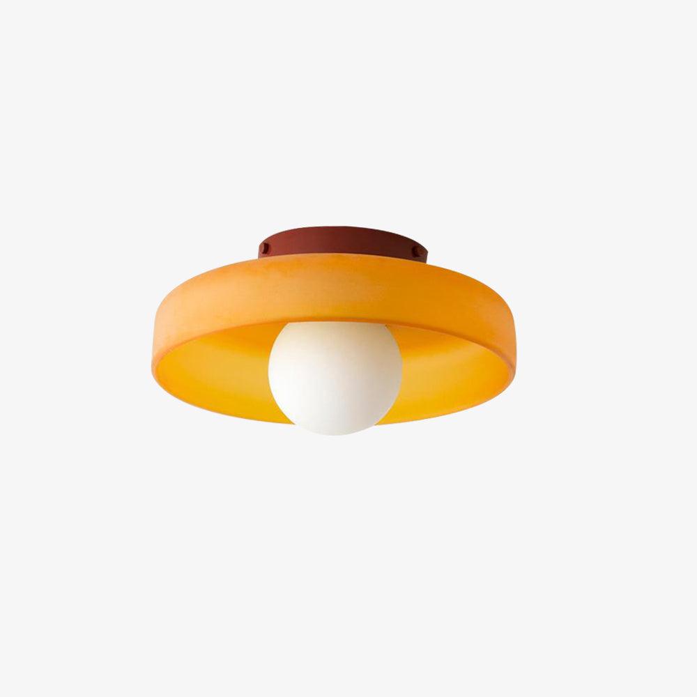 This Clérachic orange ceiling light with a maroon mounting plate, its white ball unlit against a plain wall.