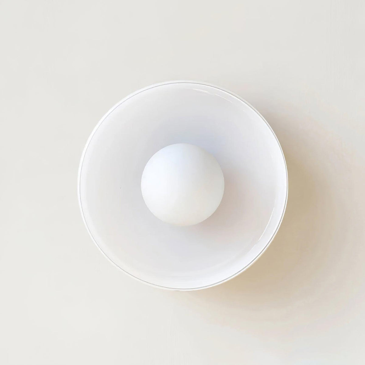 A white disc-shaped wall light with its ball centred in the ring, a different fixture from this Clérachic ceiling light.