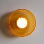 A large brown-toned wall light with its ball lit, mounted on a textured wall, a different fixture from this Clérachic ceiling light.