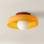 This Clérachic ceiling light in orange glass with a maroon mounting plate, its ball lit against a plain backdrop.