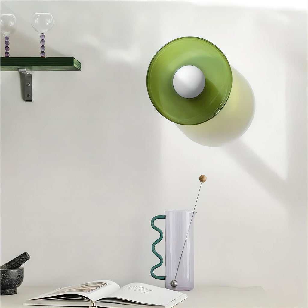 A green cylindrical wall lamp beside a vase and open book, a different fixture from this Clérachic ceiling light.