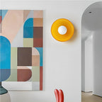 An orange disc-shaped wall light beside an abstract painting, a different mount from this Clérachic ceiling light.
