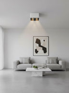 Above a living room sofa and framed print, a white two-light Clérachic spotlight glows warm on the ceiling.