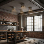 In a brick-walled kitchen, three black Clérachic spotlights cast warm light down over a wooden table.