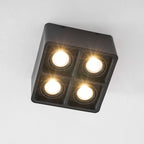 Four warm bulbs glow from this black Clérachic spotlight, angled from below against a plain white background.