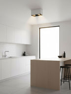 In a white kitchen with a wood island and bar stools, a black two-light Clérachic spotlight sits near the window.