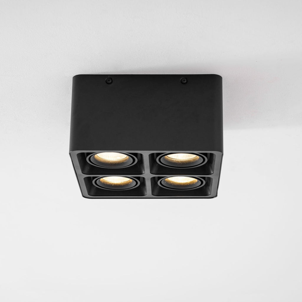 Seen face-on, this black four-light Clérachic spotlight stands unlit on a plain white background.