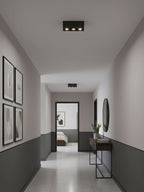 In a hallway lined with framed pictures, a black two-light Clérachic spotlight sits unlit on the ceiling.