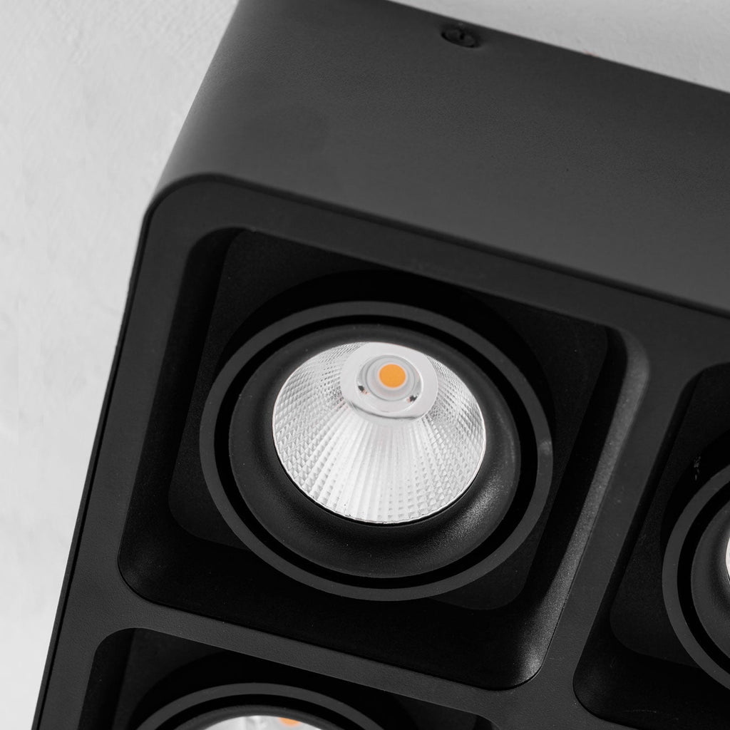 Close view of two lamp heads on this black Clérachic spotlight, warm bulbs glowing inside the ribbed reflectors.