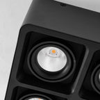 Close view of two lamp heads on this black Clérachic spotlight, warm bulbs glowing inside the ribbed reflectors.