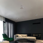 In a living room with dark curtains and a green accent chair, a white Clérachic spotlight sits unlit on the ceiling.