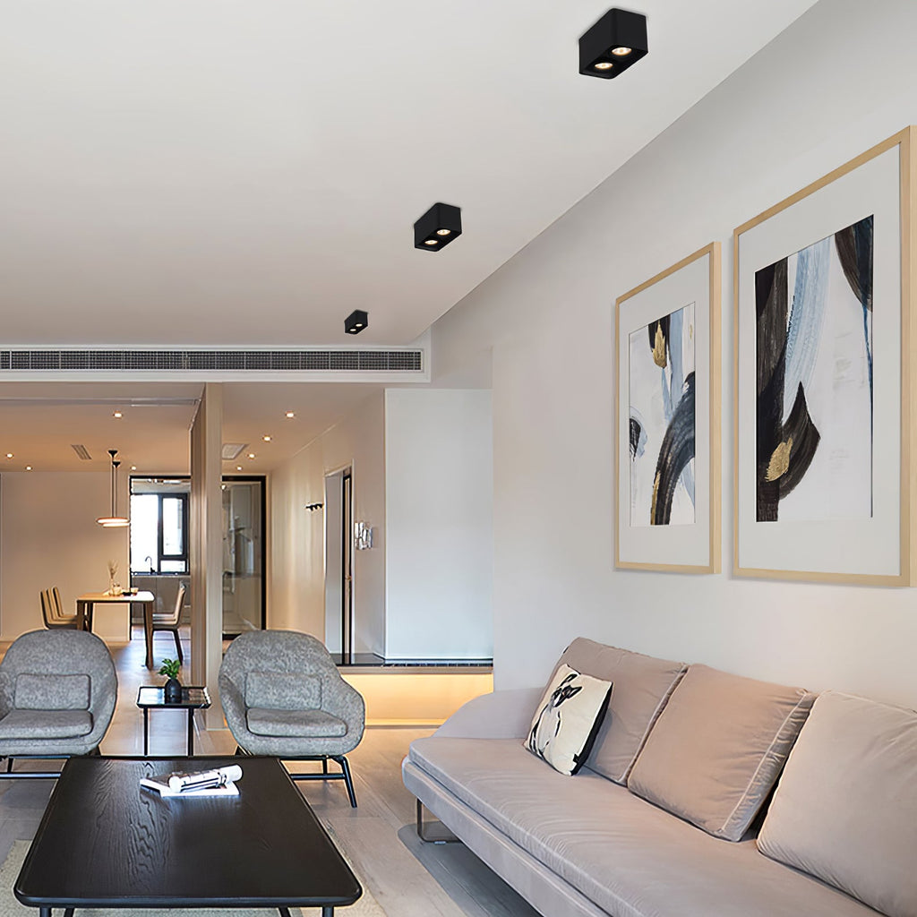 Above framed art and blue accent chairs, two black two-light Clérachic spotlights sit unlit on the ceiling.