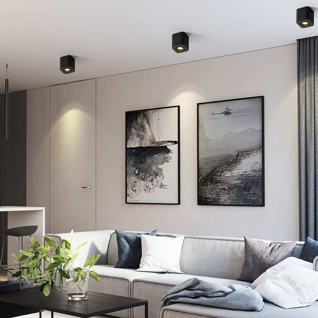 Above framed art and a sectional sofa, two black single-light Clérachic spotlights sit unlit on the ceiling.