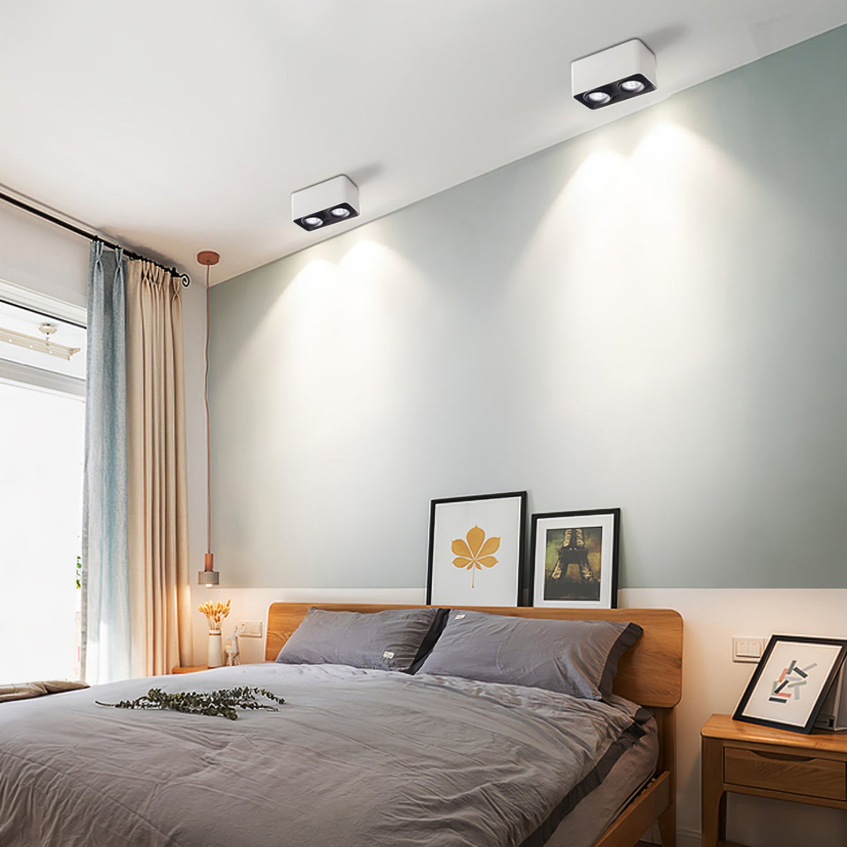 Against a sage green wall, a white two-light Clérachic spotlight glows warm above a bed.