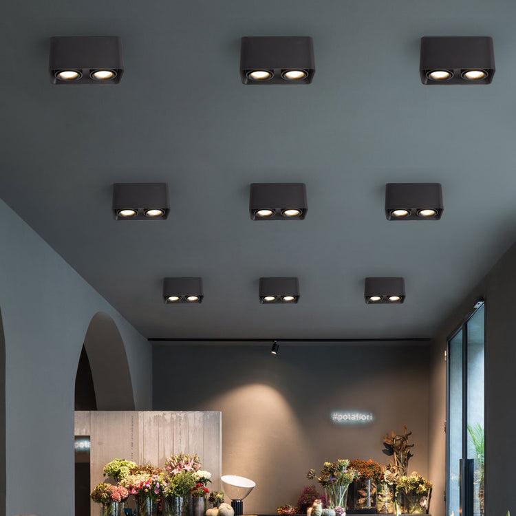 Inside a flower shop, a row of black single-light Clérachic spotlights glows warm above shelves of blooms.