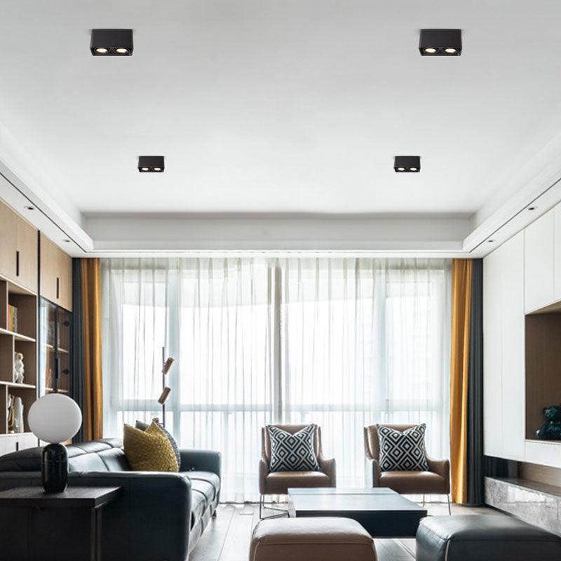 Beside floor-to-ceiling windows with sheer curtains, two black Clérachic spotlights sit unlit above a living room sofa.