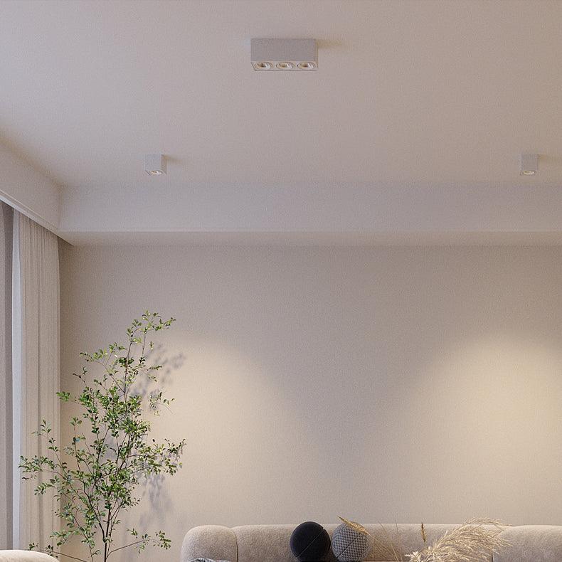 Near a potted plant and sheer curtain, two white Clérachic spotlights sit unlit on a living room ceiling.