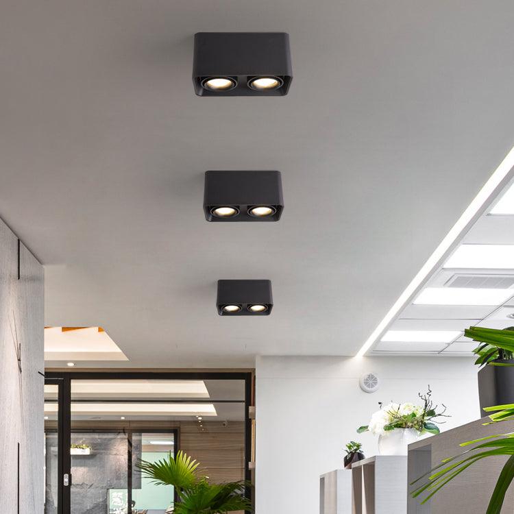 In a plant-filled lobby, three black two-light Clérachic spotlights glow warm behind a glass partition.