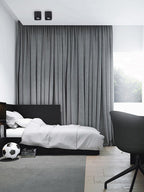 In a bedroom with grey curtains and a dark bed frame, two black Clérachic spotlights sit unlit on the ceiling.