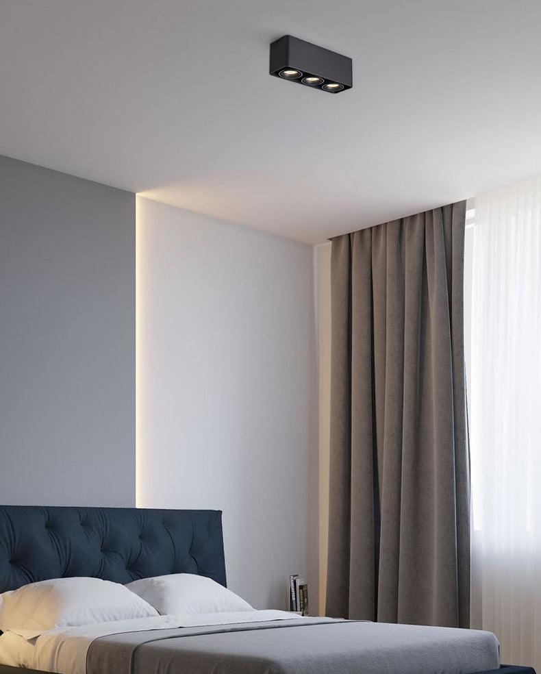 Above a bed against a teal wall, a black two-light Clérachic spotlight sits unlit beside an indirect light strip.